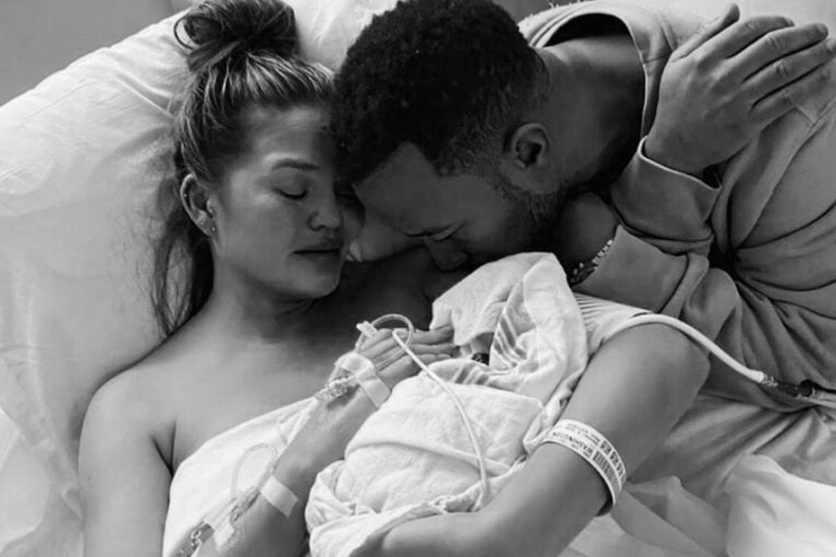 A woman lies in a hospital bed holding a newborn baby close to her chest. A man leans over from the side, resting his head on her shoulder and gently holding her arm. Both appear emotional, reminiscent of stories about celebrities who have had miscarriages, with the woman closing her eyes and the man looking downward.